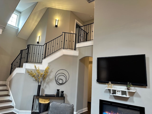 living room with a high ceiling, visible vents, baseboards, stairs, and a glass covered fireplace