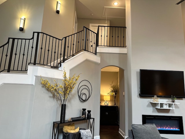 interior space with arched walkways, a high ceiling, baseboards, a glass covered fireplace, and attic access