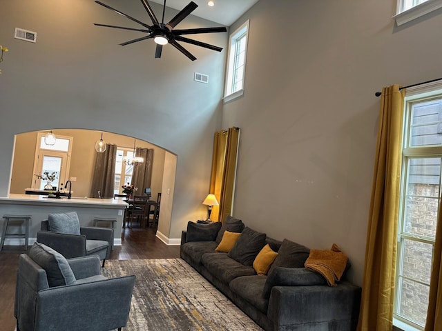 living room with a towering ceiling, visible vents, arched walkways, and dark wood-type flooring