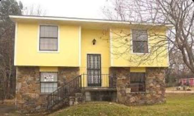 raised ranch with stone siding, a front lawn, and stucco siding