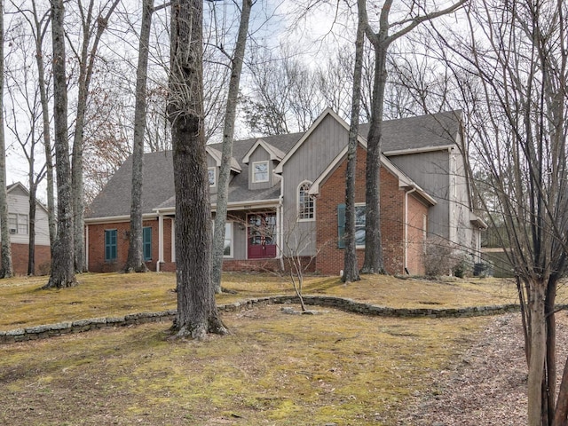 view of front of home with roof with shingles, a front lawn, and brick siding