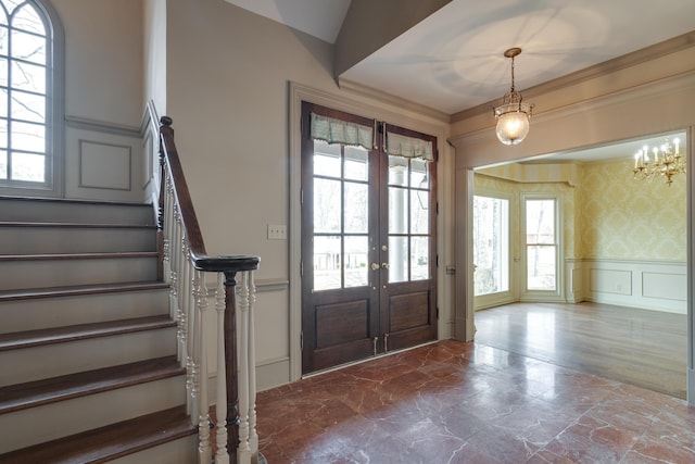 entrance foyer featuring a decorative wall, french doors, stairway, wainscoting, and wallpapered walls