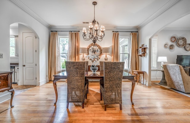 dining area with arched walkways, light wood-style flooring, and a notable chandelier