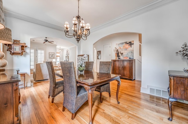 dining area with arched walkways, ornamental molding, light wood-type flooring, and visible vents