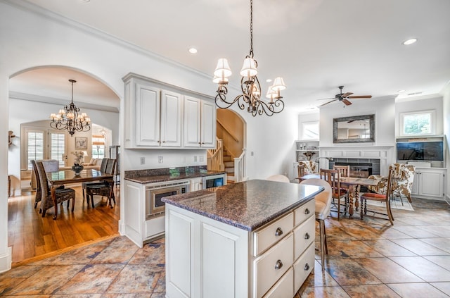 kitchen featuring arched walkways, hanging light fixtures, white cabinetry, and a center island