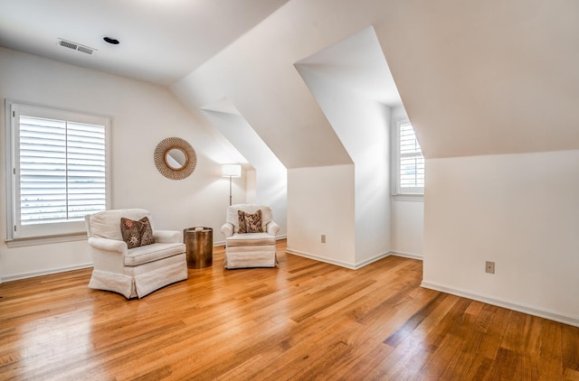 living area with lofted ceiling, visible vents, baseboards, and wood finished floors