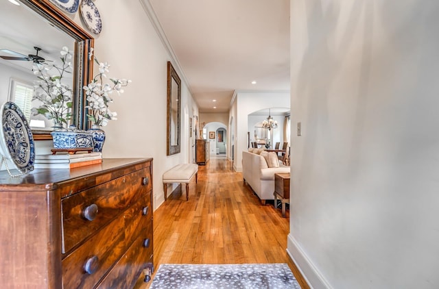 hallway with baseboards, arched walkways, ornamental molding, an inviting chandelier, and light wood-type flooring