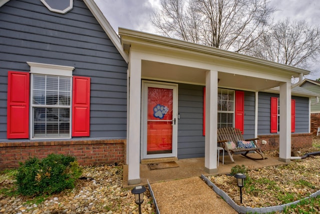 entrance to property featuring a porch and brick siding