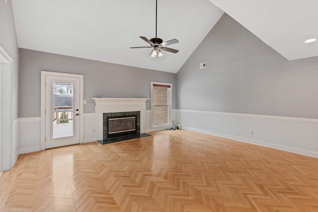 unfurnished living room with a wainscoted wall, visible vents, a high end fireplace, ceiling fan, and high vaulted ceiling