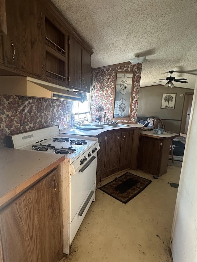 kitchen featuring a textured ceiling, dark brown cabinetry, a peninsula, a ceiling fan, and white gas range oven