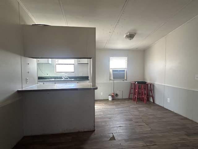 kitchen featuring dark wood-style floors, light countertops, a decorative wall, cooling unit, and a peninsula