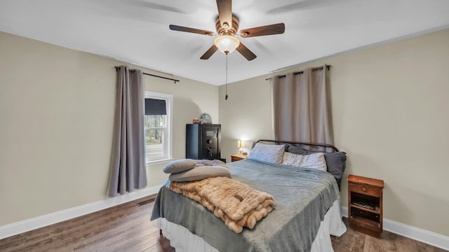 bedroom with a ceiling fan, visible vents, baseboards, and wood finished floors