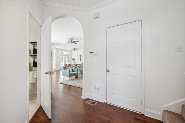 hallway featuring arched walkways, crown molding, visible vents, dark wood-type flooring, and baseboards