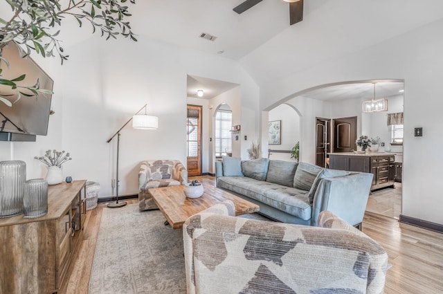 living room with arched walkways, baseboards, visible vents, and light wood finished floors