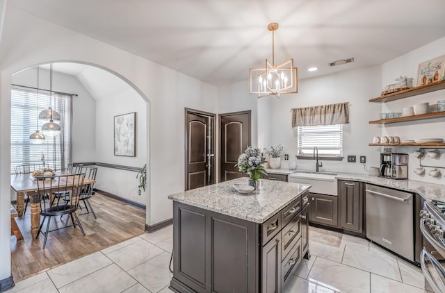 kitchen featuring light stone counters, a center island, pendant lighting, appliances with stainless steel finishes, and a sink