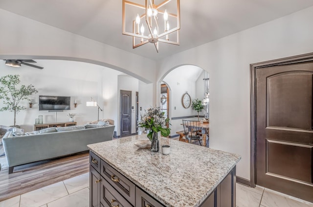 kitchen featuring a center island, arched walkways, hanging light fixtures, open floor plan, and light stone countertops