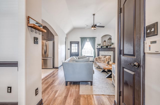 living room featuring arched walkways, lofted ceiling, ceiling fan, a stone fireplace, and light wood-type flooring