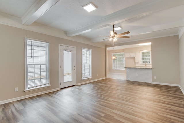 unfurnished living room with light wood-style floors, beam ceiling, a textured ceiling, and a ceiling fan