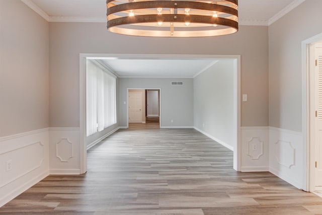 unfurnished room with visible vents, wainscoting, light wood-type flooring, beam ceiling, and crown molding