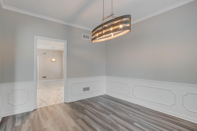 empty room featuring visible vents, wood finished floors, crown molding, and wainscoting