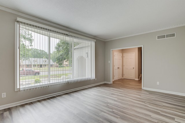 spare room with baseboards, visible vents, wood finished floors, a textured ceiling, and crown molding