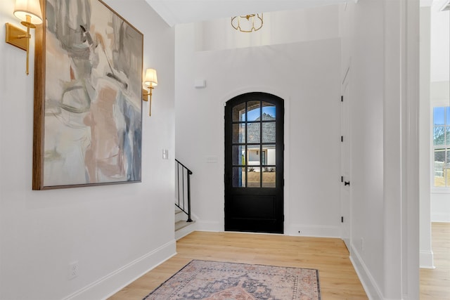 foyer with arched walkways, stairway, light wood-style flooring, and baseboards