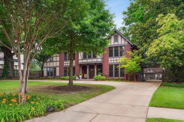 tudor-style house with brick siding, a front yard, fence, and a gate