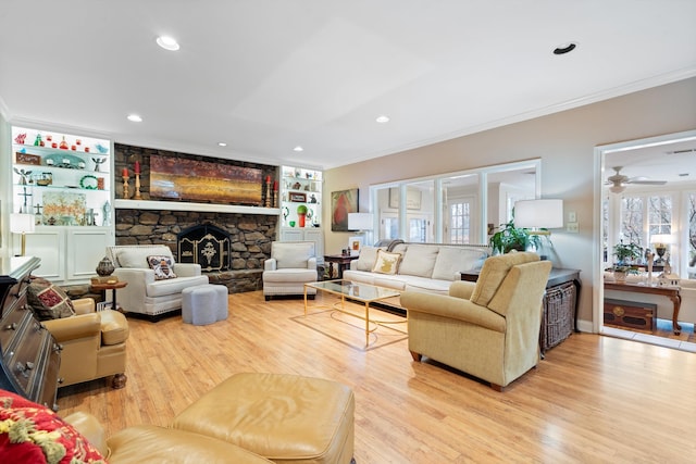 living area featuring light wood-type flooring, built in shelves, ornamental molding, and a stone fireplace