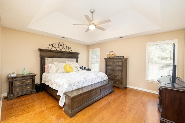 bedroom featuring baseboards, visible vents, a raised ceiling, and wood finished floors