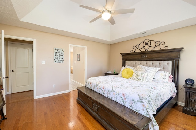 bedroom featuring light wood-style floors, a raised ceiling, visible vents, and baseboards