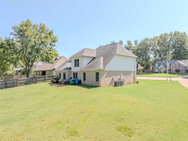 back of house featuring brick siding, fence, central AC, and a yard