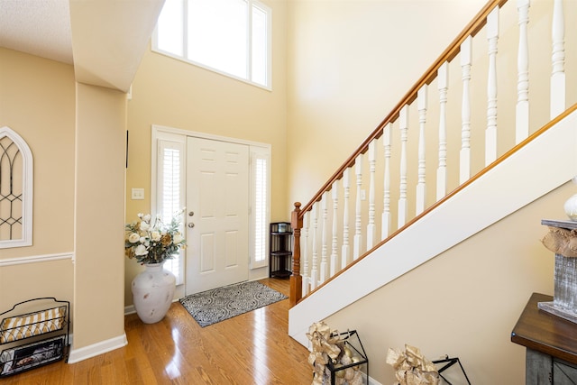 foyer entrance with a high ceiling, stairway, wood finished floors, and baseboards