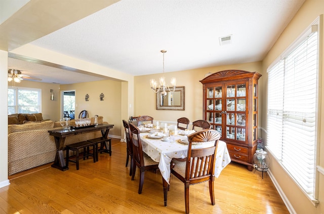 dining space featuring ceiling fan with notable chandelier, light wood-type flooring, visible vents, and baseboards