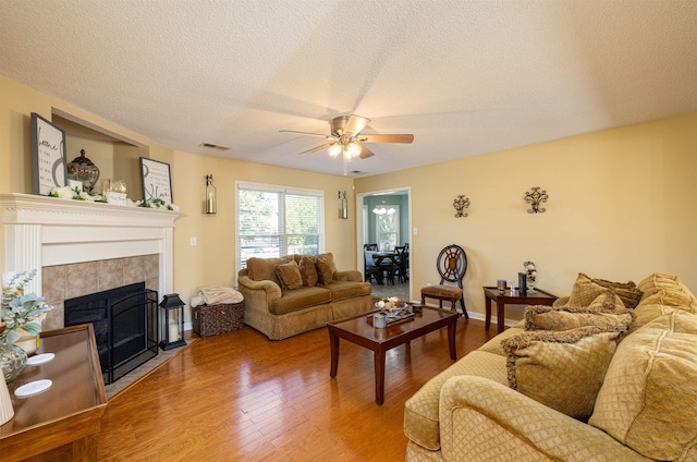 living area with a fireplace, a ceiling fan, a textured ceiling, wood finished floors, and baseboards