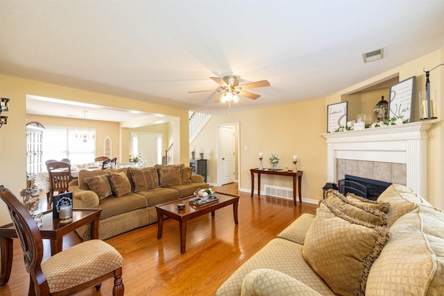 living area with a tile fireplace, ceiling fan with notable chandelier, wood finished floors, visible vents, and baseboards