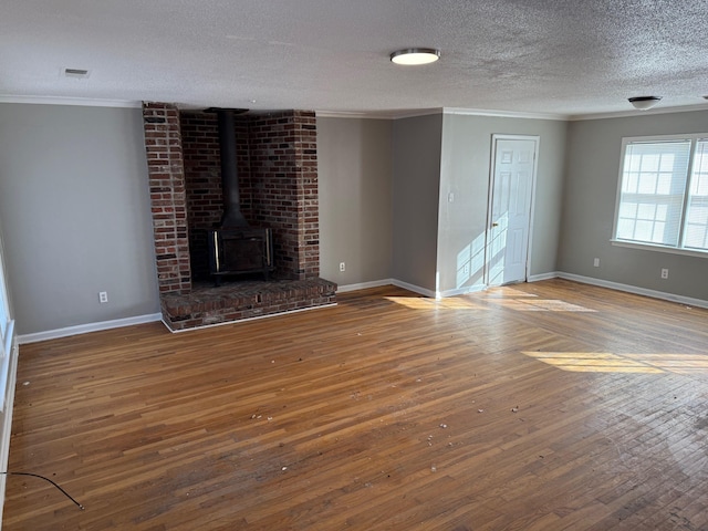 unfurnished living room with ornamental molding, a wood stove, a textured ceiling, wood finished floors, and baseboards