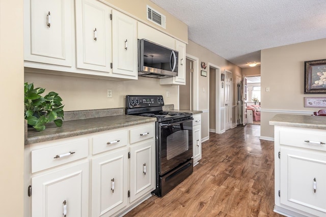 kitchen featuring dark countertops, stainless steel microwave, white cabinetry, a textured ceiling, and black range with electric cooktop