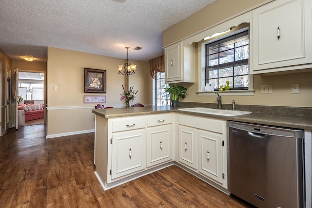 kitchen featuring dark countertops, stainless steel dishwasher, white cabinets, a sink, and a peninsula