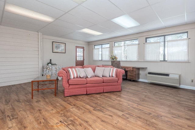 living room with a paneled ceiling, a wall mounted air conditioner, and wood finished floors