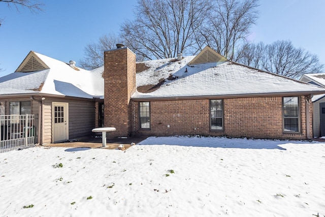 snow covered rear of property featuring brick siding, fence, and a chimney