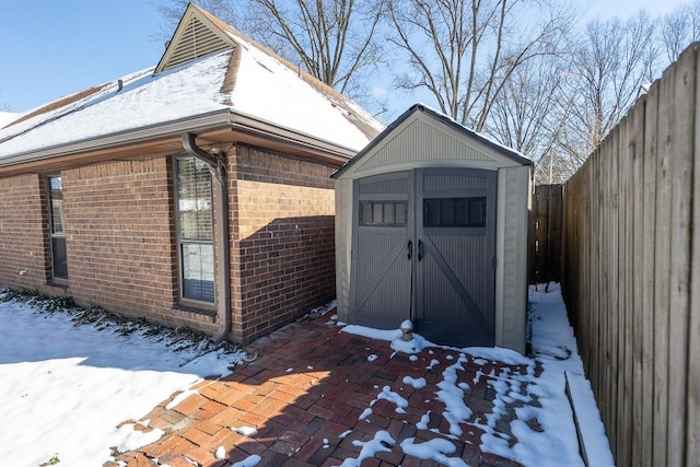 snow covered structure featuring an outdoor structure, a storage shed, and fence