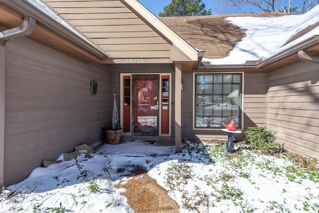 snow covered property entrance with a shingled roof