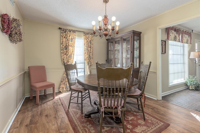 dining space with a chandelier, ornamental molding, dark wood-style flooring, and a textured ceiling