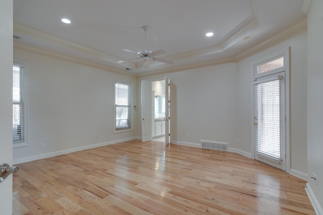 empty room featuring light wood-style floors, a tray ceiling, a wealth of natural light, and visible vents