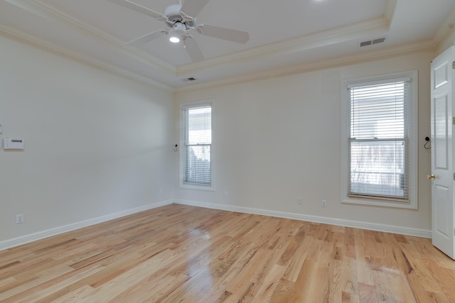 empty room with visible vents, baseboards, light wood-style floors, a raised ceiling, and crown molding