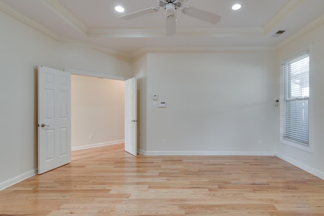 spare room with light wood finished floors, a raised ceiling, and crown molding