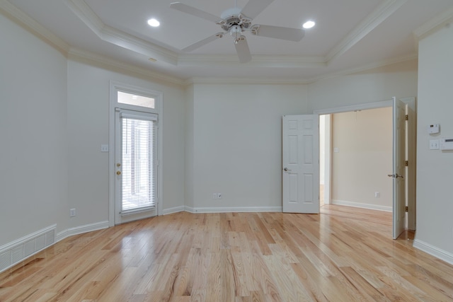 empty room with light wood-type flooring, a tray ceiling, visible vents, and ornamental molding