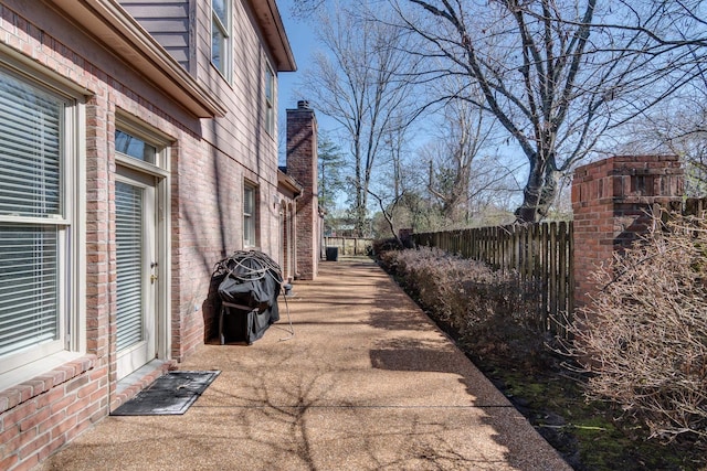 view of home's exterior with brick siding, a chimney, and fence