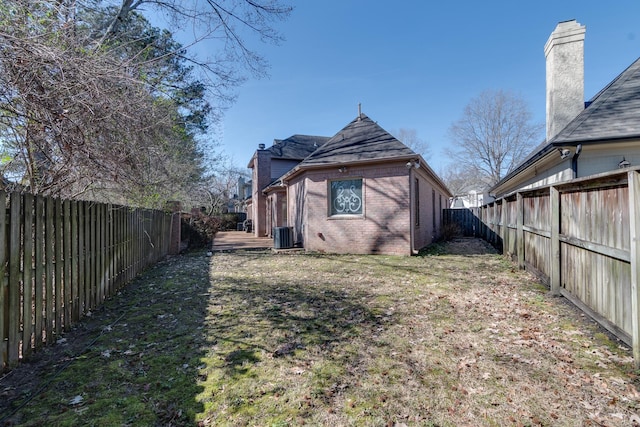 exterior space with a yard, brick siding, a chimney, and a fenced backyard