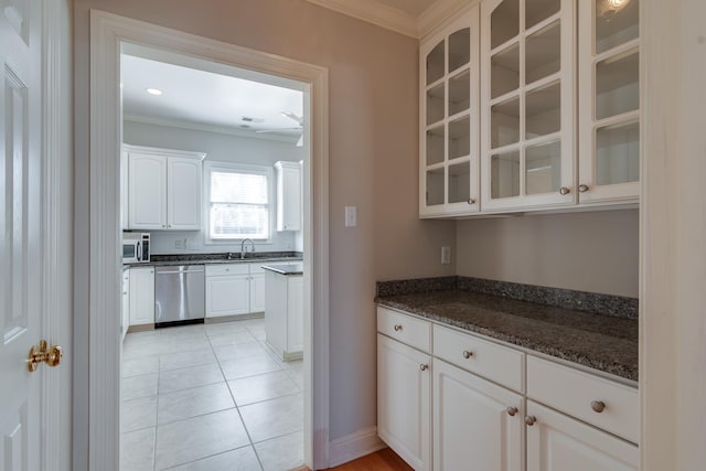 kitchen with dark stone counters, glass insert cabinets, appliances with stainless steel finishes, ornamental molding, and white cabinetry